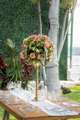 Arreglo floral sobre una mesa de madera con cristalería montada en un jardín para un evento social en Mexico