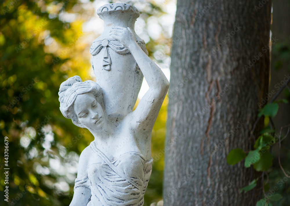 Sticker sculpture of a girl in the spring park. An old statue in a park of a sensual semi-nude Greek or Italian Renaissance woman with a vase in a city park. sunny day in the summer garden. close-up