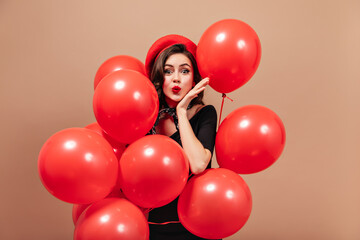 Elegant girl in red beret and black dress blows kiss and holds huge balloons