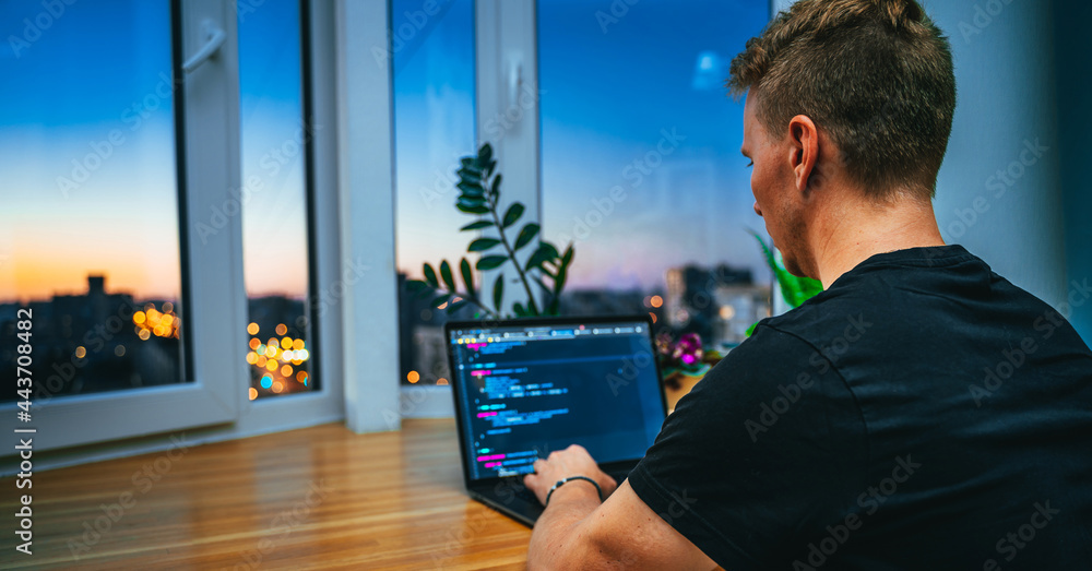 Canvas Prints a young male developer is programming a code script late at night with beautiful city lights at nigh