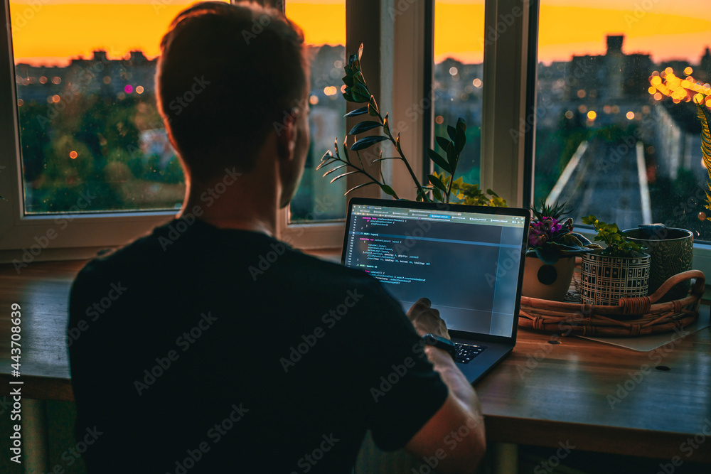 Canvas Prints a young male developer is programming a code script late at night with beautiful city lights at nigh
