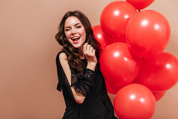 Cool brunette girl in elegant blouse holds bright balloons and winks on isolated background