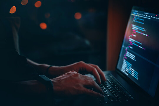 The code is on a laptop on a wooden table in front of the window  in the dark with a view of the lights of the night city, color lighting in the room, home decor	