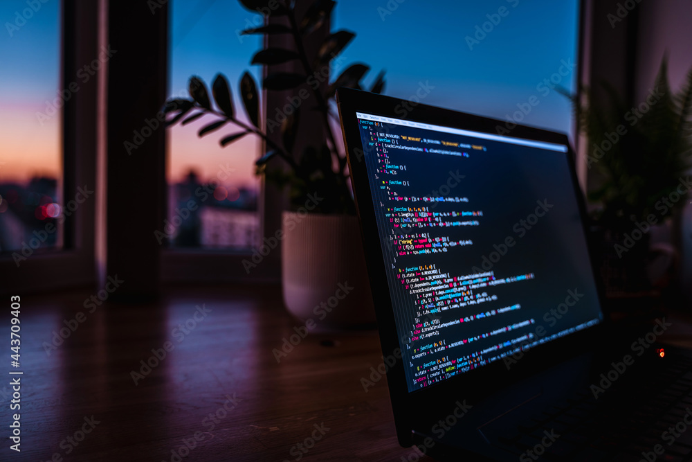 Wall mural the code is on a laptop on a wooden table in front of the window in the dark with a view of the ligh