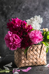 Beautiful peonies in wicker basket on wooden table