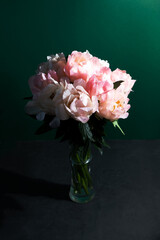 A bouquet of coral peonies in a glass vase on a dark green background. Greeting card
