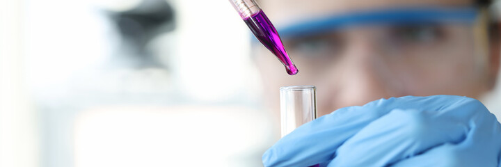 Researcher drips purple liquid from pipette into test tube