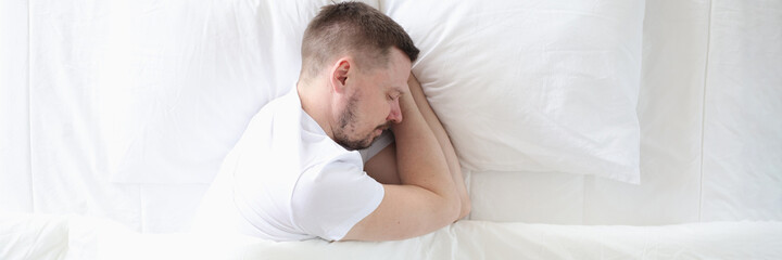 Young man is sleeping peacefully on large white bed