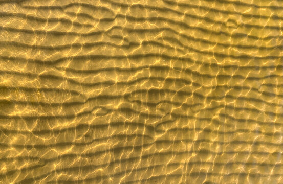 A horizontal pattern of golden sand created by waves on the coast of the resort in Estonia. Beautiful natural ornament of sand ripples on shallow water on the Baltic Sea coast. Solar glare on water.