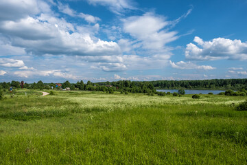 A rural landscape with a field and a river and a beautiful cloudy sky.