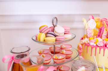 French macaroons on a cake stand .Candy bar with macaron, cakes, cheesecakes, cake pops.Colorful macaroons on serving tray.Decorative sweet birthday table in bright colors of yellow, white and pink.