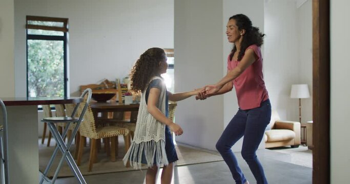 Happy mixed race mother and daughter dancing in living room