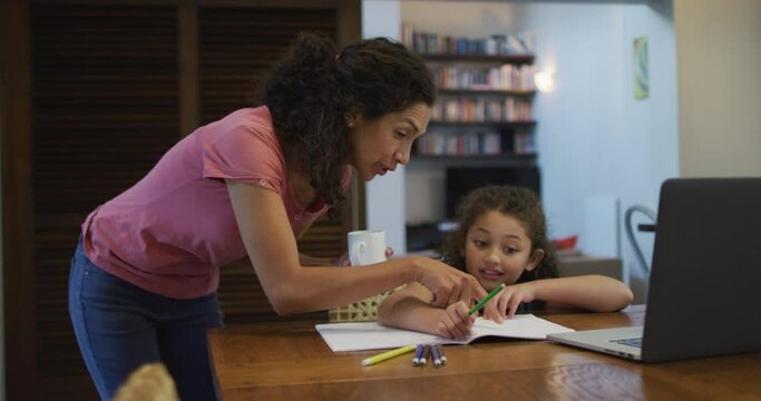 Happy mixed race mother and daughter doing homework together at home