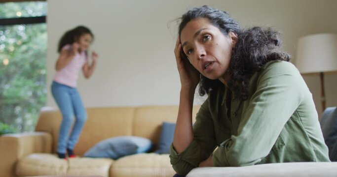 Mixed race daughter jumping on the sofa, mother is stressed