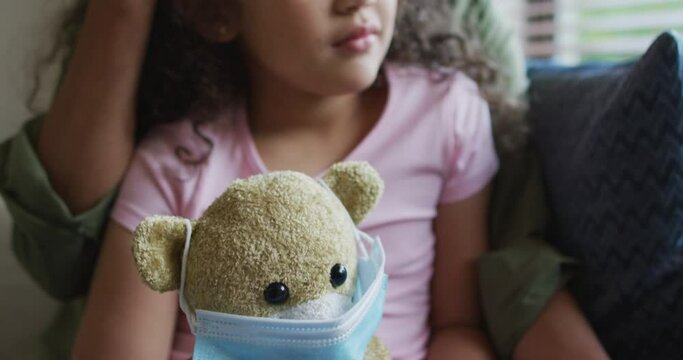 Mixed race mother and daughter hugging,daughter holding tedy bear with face mask