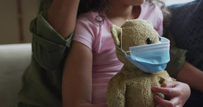 Mixed race mother and daughter hugging,daughter holding tedy bear with face mask