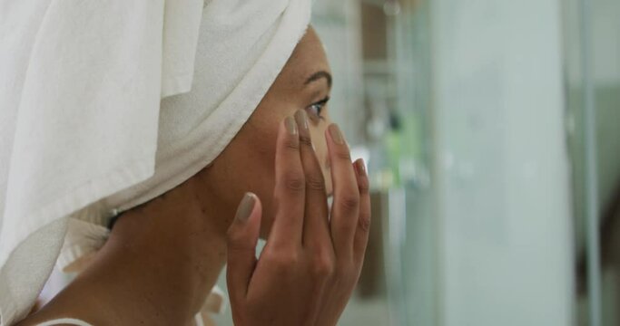 Mixed race woman wearing towel on head applying cream on her face