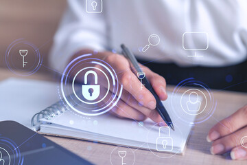 Businesswoman is taking notes of clients needs to protect cyber security from hacker attacks and save clients confidential data. Padlock Hologram icons over the typing hands. Formal wear