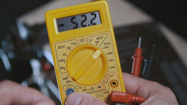 A man changes multimeter knob position to detect malfunctions in the printed circuit board. The device that measures voltage, amperage, shorts shows digits in its screen. 