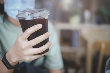 Hand holding a glass of iced black coffee with wearing face mask in the morning..