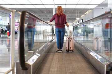 woman passenger with luggage in international airport or modern train station walking to gate.