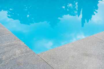 stone corner of blue swimming pool  and reflection trees and sky can be seen in water