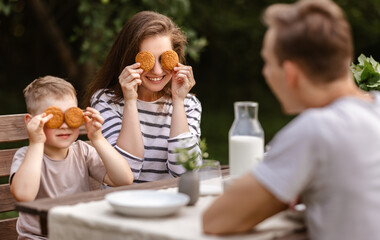 Family lunch: mother father and child boy laugh and eat cookies with milk in the summer in the garden