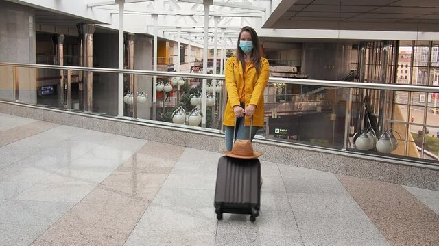 happy modern tourist woman in yellow jump with face medical mask and luggage at the airport station. happiness to travel again, opening borders for tourism. new normal for travelers