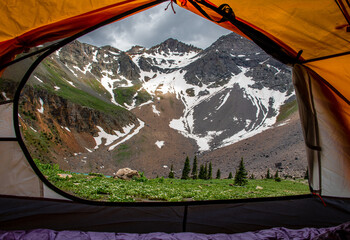 View of a mountain peak with snow on it through an orange camping tent at Blue lakes in Colorado. 
