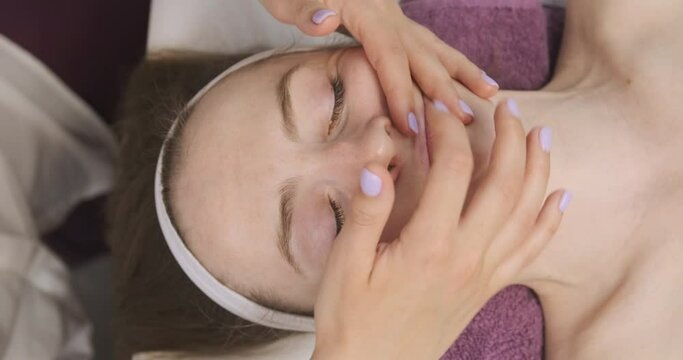 Facial massage, nasal fold area. Hands of the masseur gently make a modeling facial massage. Young woman in a beauty salon