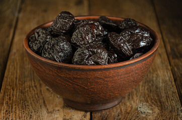 Dried prunes in a ceramic folk bowl on a wooden table.
