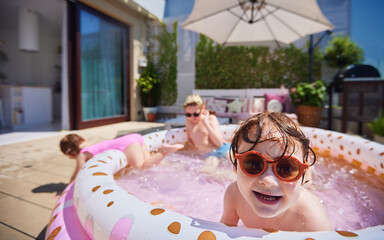excited kids having fun in inflatable swimming pool at home patio at sunny summer day