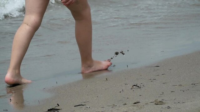 Closeup of child feet walking on the sandy sea shore beach, slow motion