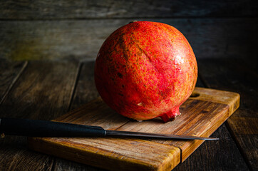 Red ripe pomegranate on a kitchen board with a knife. Ripe healthy fruit. Cooking in the kitchen.