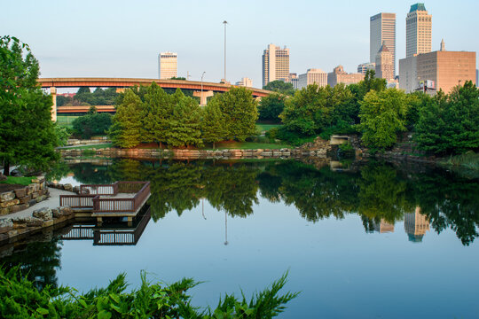 Morning photo of beautiful Centennial Park in Tulsa, OK with the downtown skyline in the background and reflecting on the pond.