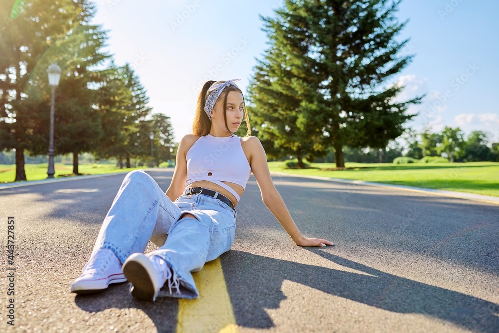 Wall mural Fashionable trendy teenage hipster female sitting on road in park