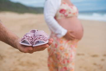 Hand holding newborn's shoes at the beach