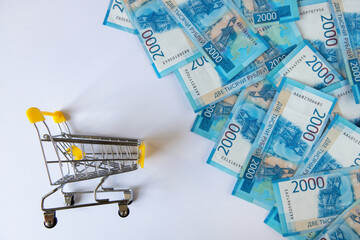 2000 rubles bills near mini shopping cart on white background, top view, flat lay. Finance concept, buying currency, business. Paper money, offline purchases. Horizontal