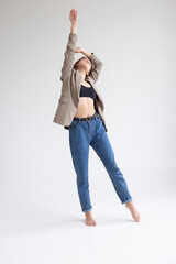 portrait of young caucasian attractive woman with long brown hair in blue jeans, black top and suit jacket on white background. skinny pretty lady posing at studio with bare feet