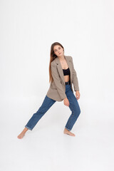 Fototapeta na wymiar portrait of young caucasian attractive woman with long brown hair in blue jeans, black top and suit jacket on white background. skinny pretty lady posing at studio with bare feet