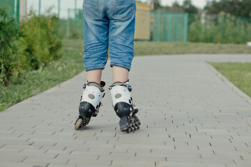 Little boy in protective equipment and rollers stands on walkway in park, low angle view