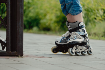 Little boy in protective equipment and rollers stands on walkway in park, low angle view