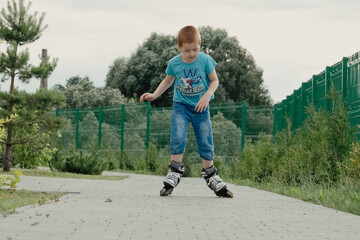 Little boy in protective equipment and rollers stands on walkway in park, low angle view