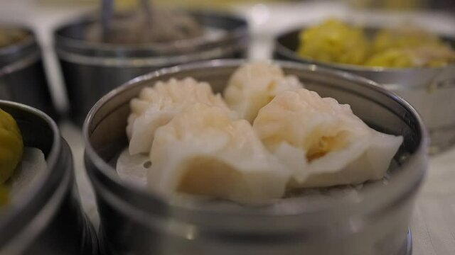 This close up video shows a delicious dish of shrimp dumpling ha gow with a dim sum feast in the background.