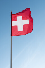 Swiss flag waving in wind. Flag of Switzerland on blue sky background.