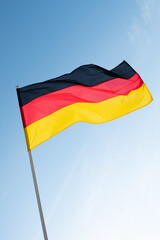 German flag waving in wind. Flag of Germany on blue sky background.