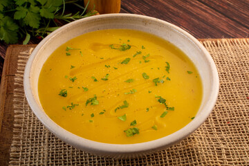 Hot cassava cream broth in a white bowl, on a wooden table (Brazilian caldo de mandioquinha)