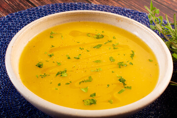 Hot cassava cream broth in a white bowl, on a wooden table (Brazilian caldo de mandioquinha)