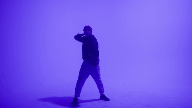 Young blonde guy dancing modern choreography on purple background in studio. Talented choreographer man showing the new hip hop movements. Shooting a dance video clip. Hip hop school for teenagers. 