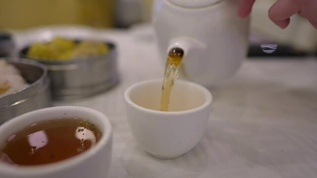 This close up video show fresh hot tea being poured by an anonymous hand into small cups at a dim sum restaurant.